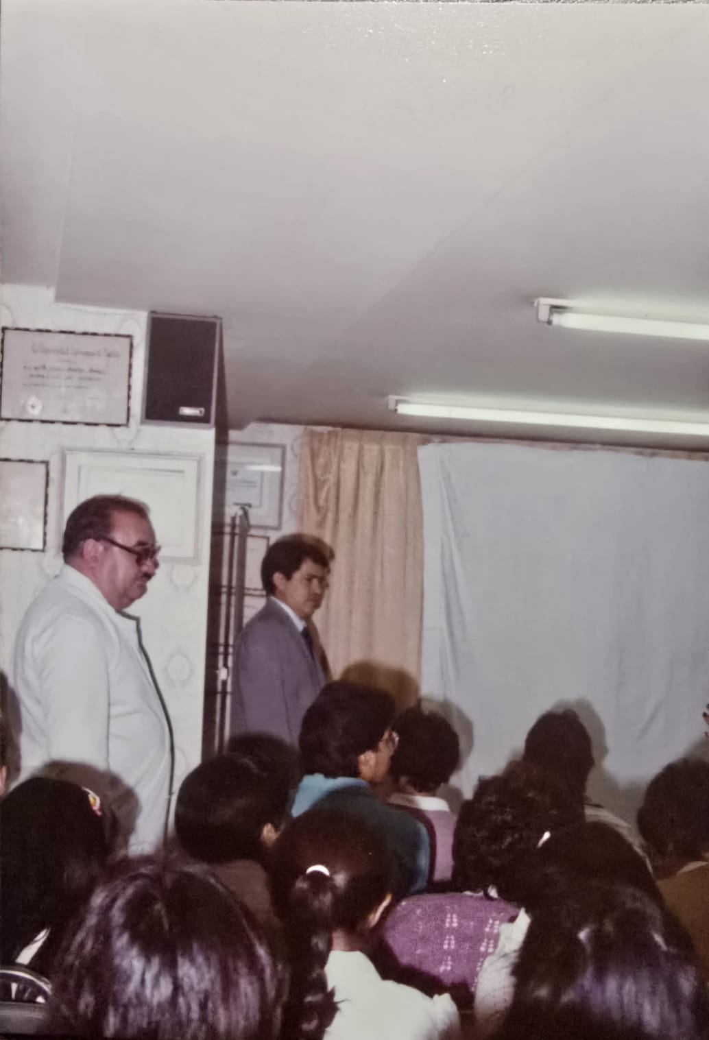 Profesor Dr. Francisco Arellano Ocampo enseñando dermatología a jóvenes médicos en formación en la Clínica Dermatológica de Puebla, con diplomas universitarios visibles al fondo. Maestro formador de generaciones de dermatólogos en Puebla desde 1971.